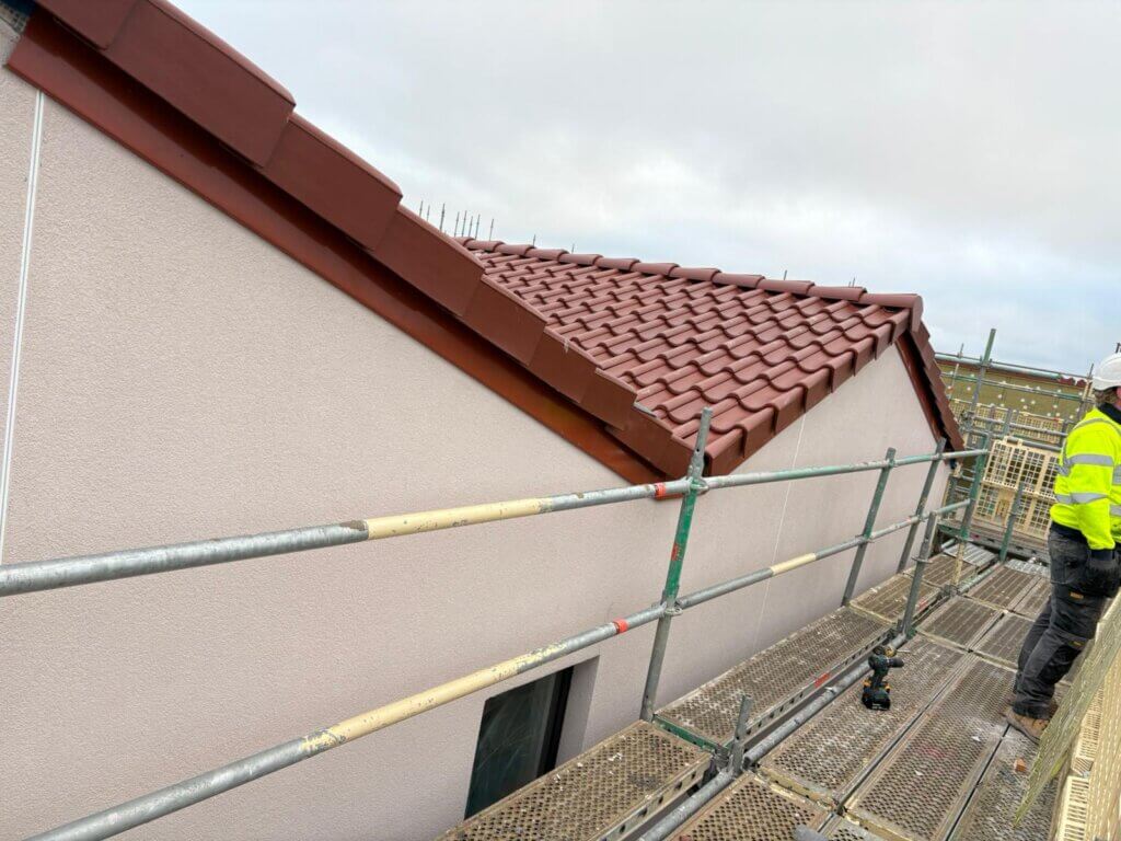 Roofline view from scaffolding walkway showing red slate roof tiles and cream rendered wall during rainwater installation