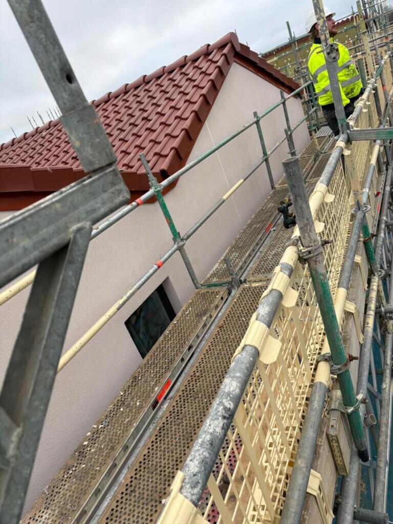 "Close-up perspective from scaffolding platform of red slate roofing over cream veneer cladding on residential property