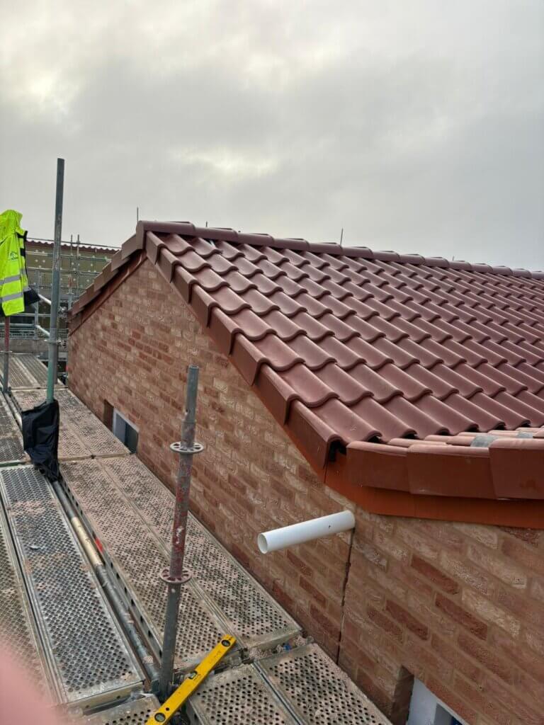 Scaffolding walkway view of red slate roof tiles meeting red brick wall on housing development