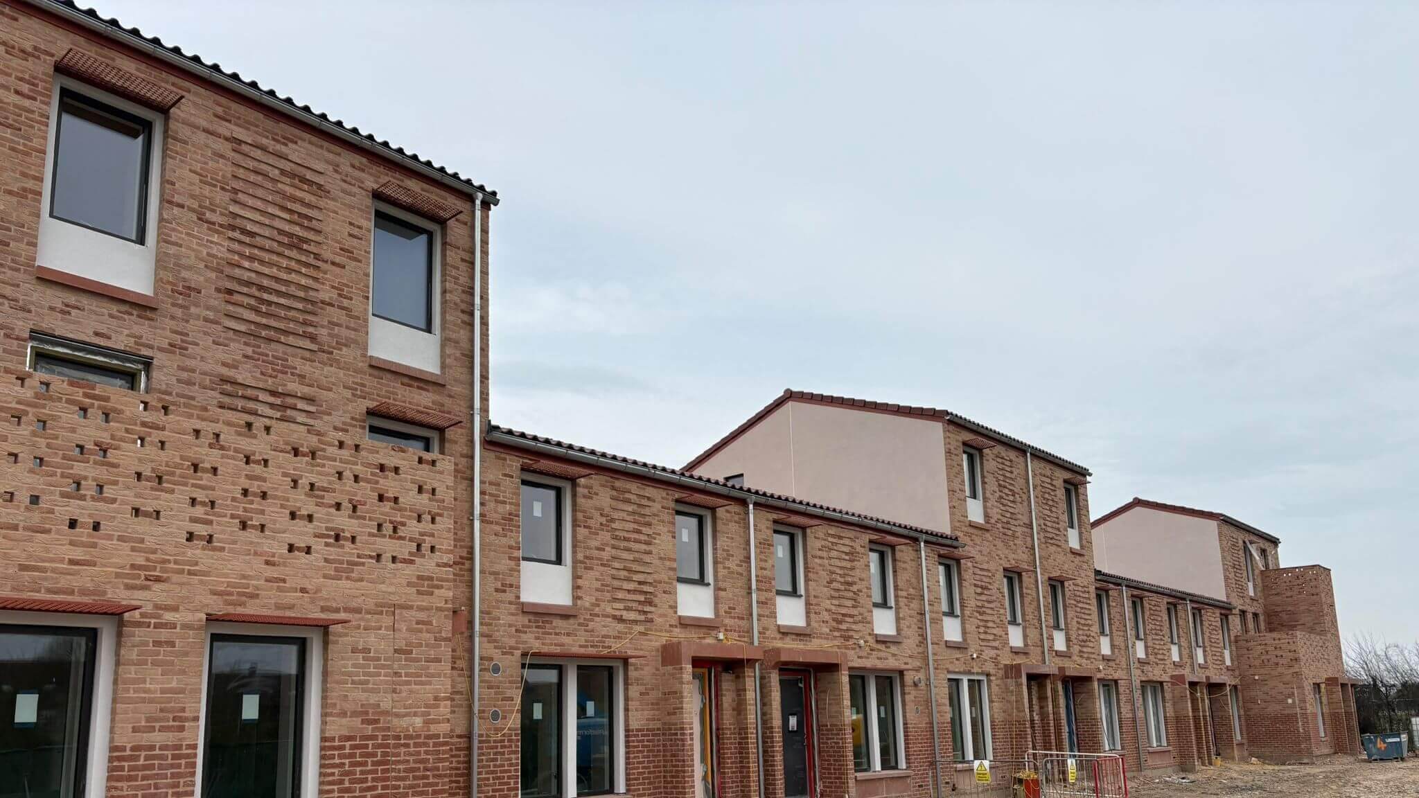 Freshly installed galvanised steel guttering and downpipes running along a row of new build houses under overcast sky