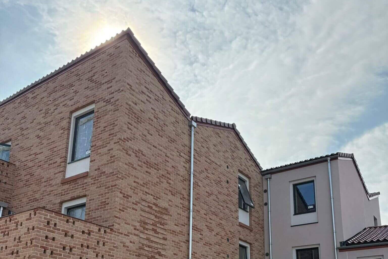 Ground-level view looking up at newly installed galvanised steel hopper heads and downpipes on adjacent houses, one with red brick walls and one with cream rendered veneer