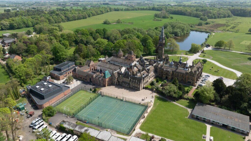 Aerial view of Scarisbrick Hall School, Ormskirk, showing the Grade I listed Victorian Gothic main building alongside modern new-build theatre and teaching facilities, Lancashire countryside setting.