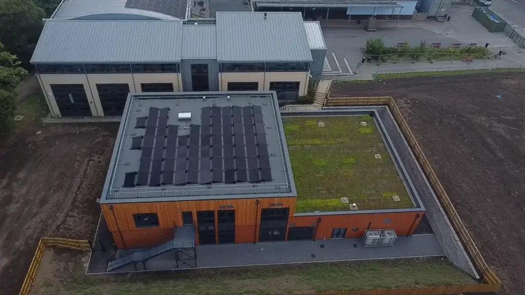 Aerial view of new-build teaching block at Immanuel College, Bradford, showing flat roof with solar panels and sedum green roof, timber cladding facade, and aluminium parapet cappings throughout.