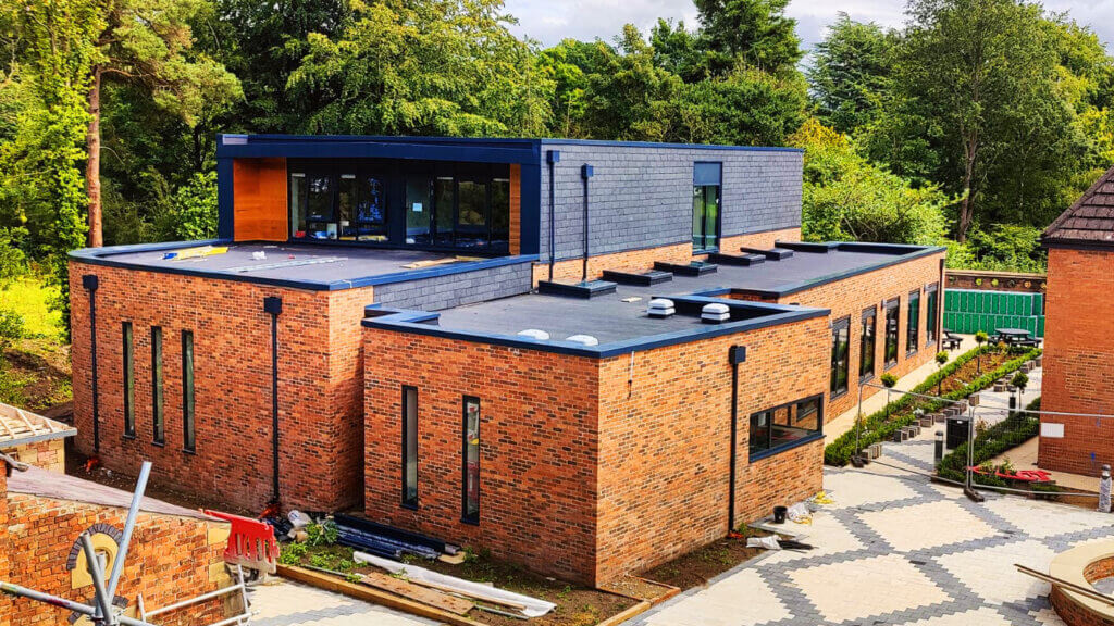 New-build theatre and teaching facilities at Scarisbrick Hall School, Ormskirk, under construction, showing aluminium parapet cappings to flat roof perimeters and downpipes throughout.