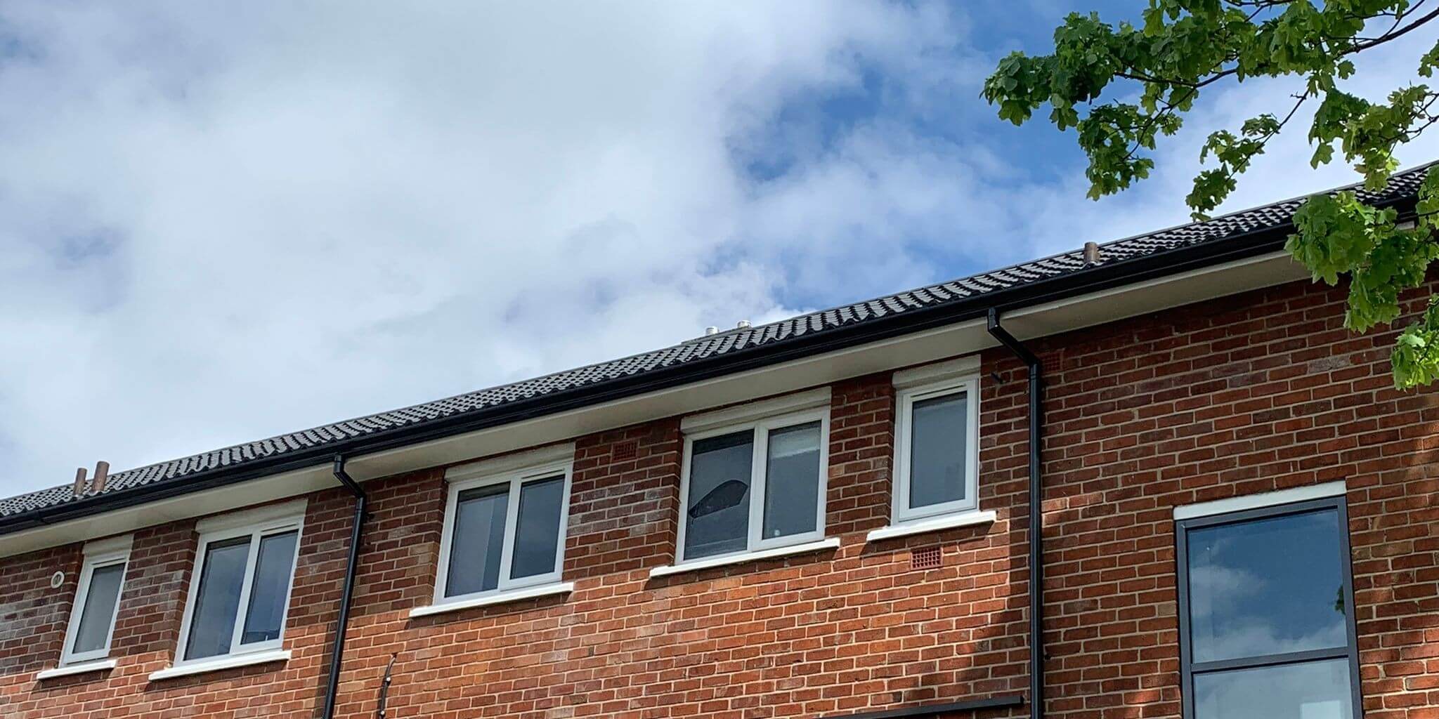 Black uPVC guttering and downpipes installed on a post-war social housing block as part of a 500-home estate regeneration programme in Blackburn