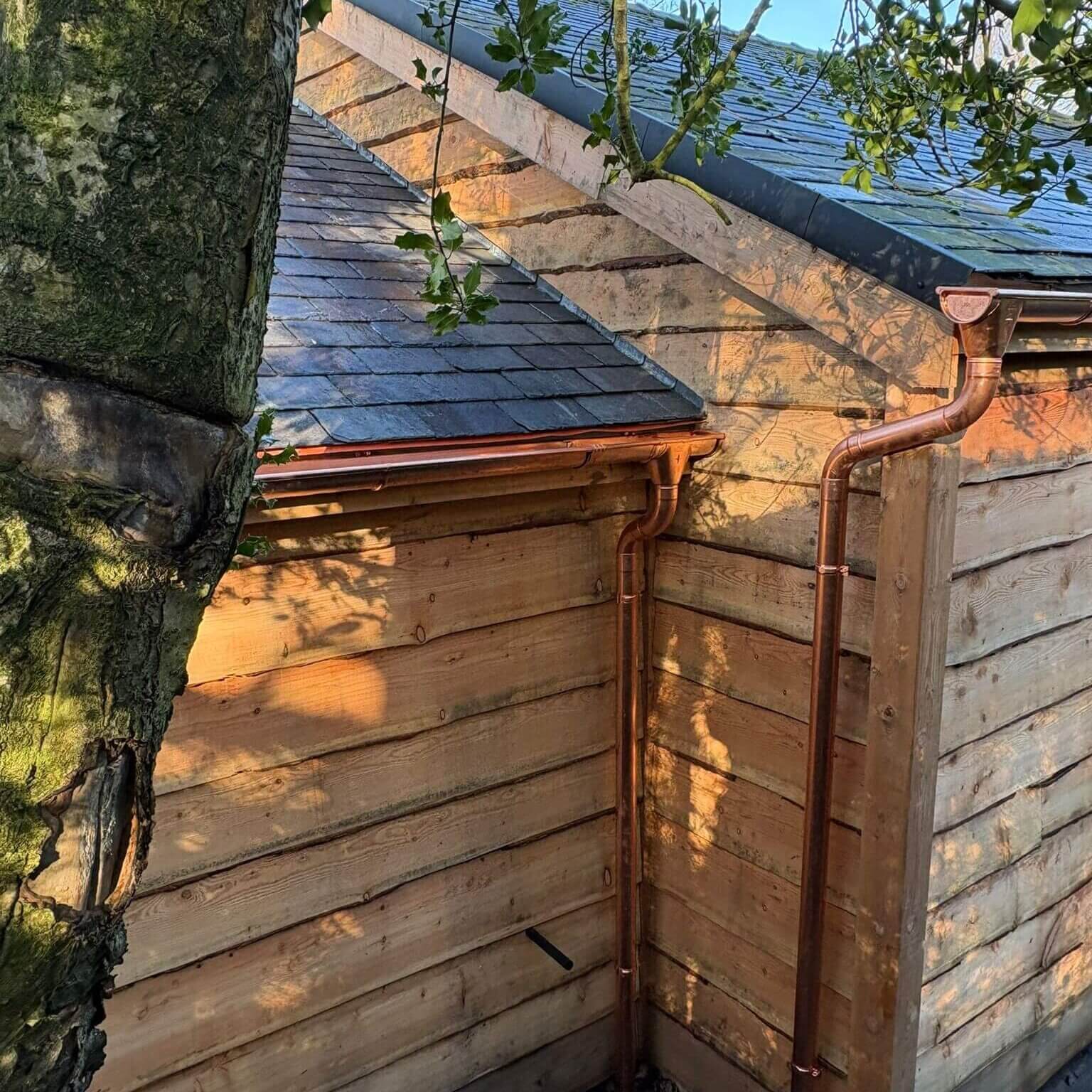 Copper rainwater systems at the corner junction of a pool house roof at a Grade II listed country house in Lancashire — half-round gutters and round downpipe against slate roof