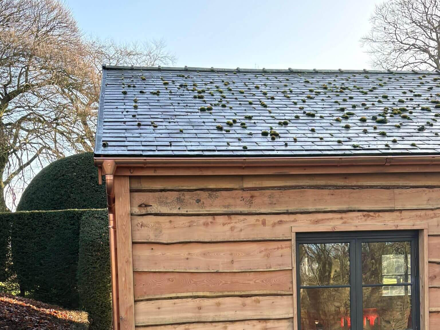 Copper half-round gutter and round downpipe on the gable end of a pool house at a Grade II listed country house in Lancashire, with slate roof above