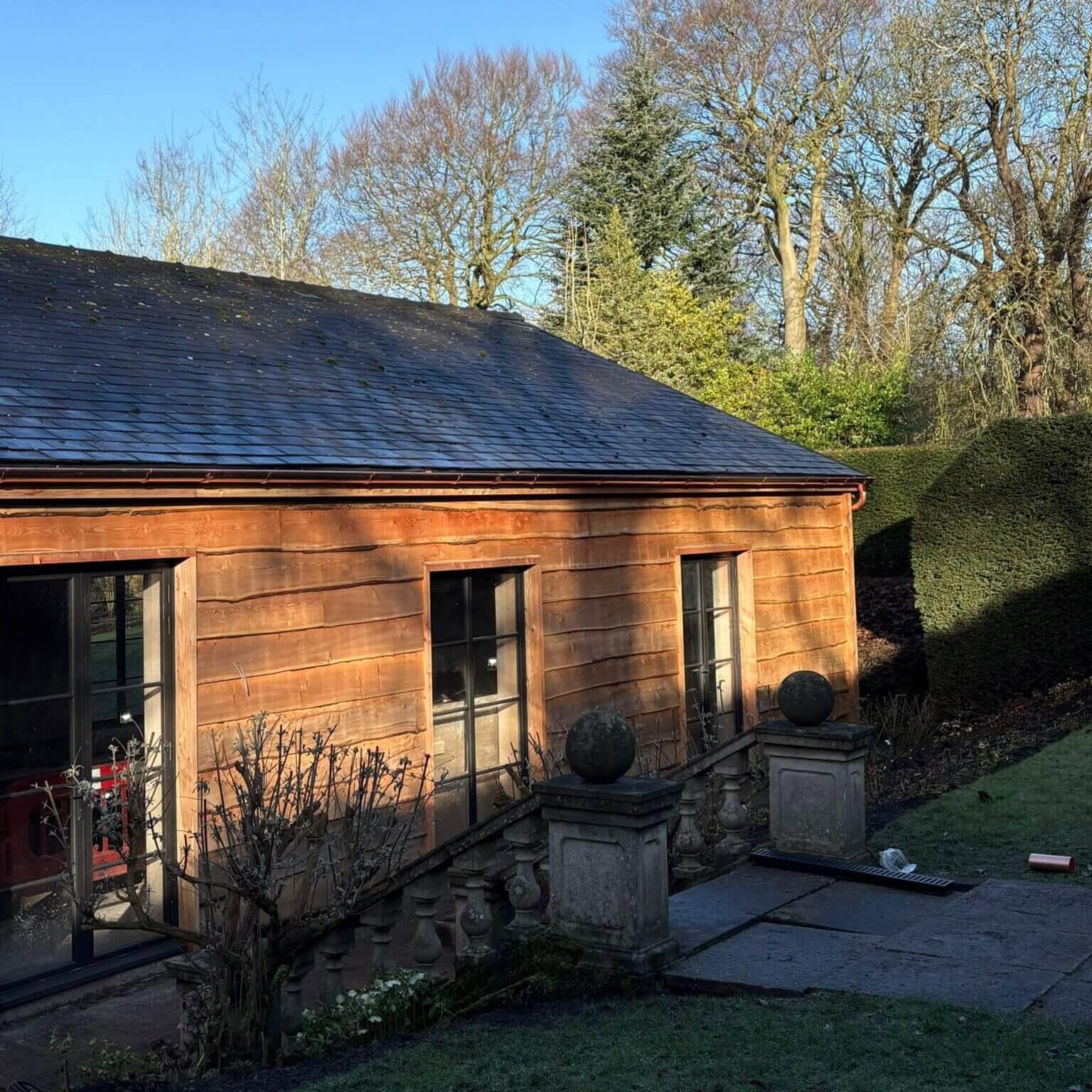 Copper half-round gutters running along the eaves of a timber-clad pool house at a Grade II listed country house in Lancashire, against a slate roof