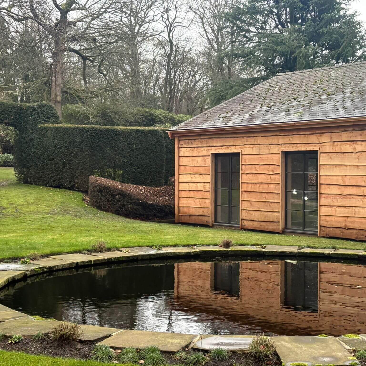 New copper half-round gutters installed on a timber-clad pool house at a Grade II listed country house in Lancashire, with ornamental pond in the foreground