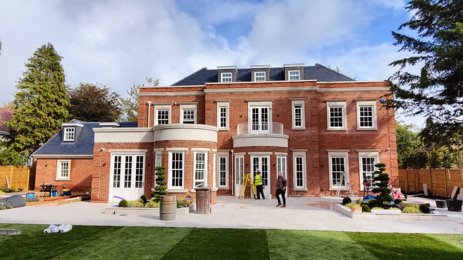 White aluminium rainwater goods and downpipes on a high-specification red brick detached house under construction, with slate roof and Georgian-style architectural detailing