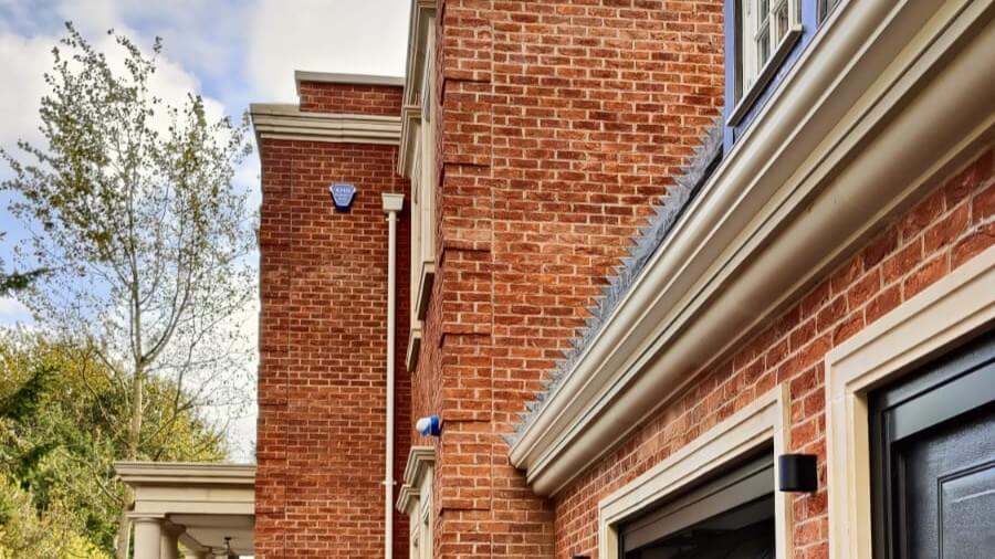 White aluminium ogee-profile gutter on a high-specification red brick detached house, with rendered cornice and architectural stone detailing